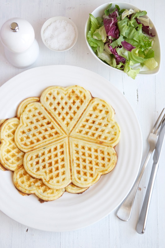 two savoury waffles on white plate with cutlery, salt and pepper