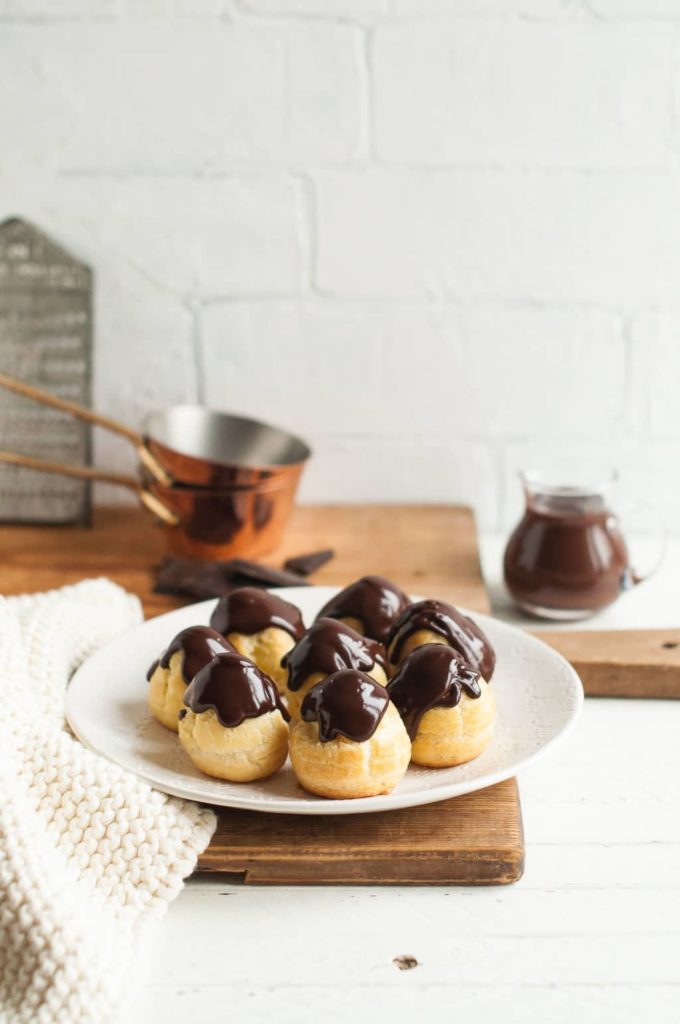 profiteroles with chocolate ganache on white plate with knitted cloth