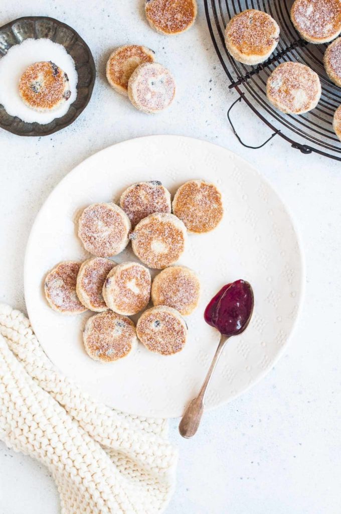 welsh cakes on a white plate with jam and a knitted cloth underneath