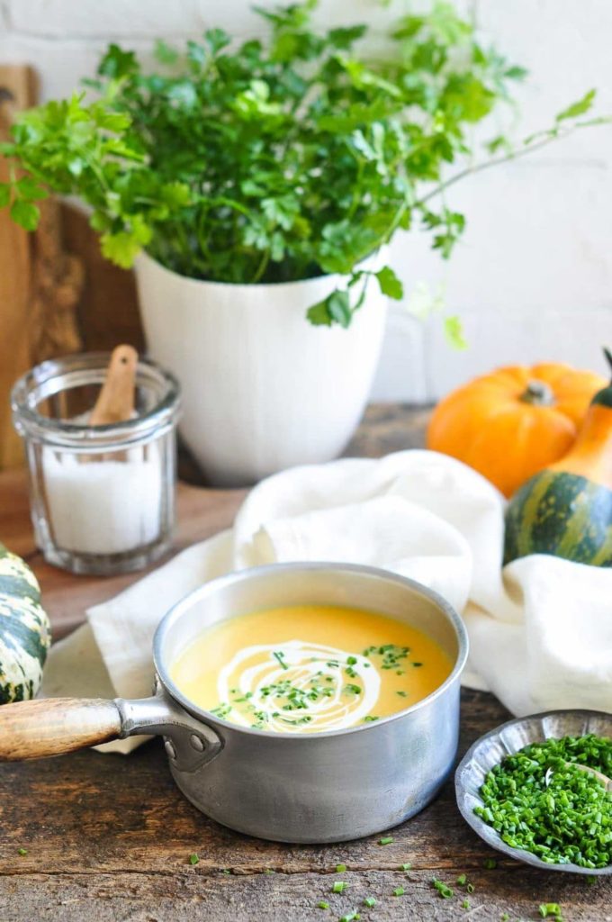 roast pumpkin soup in saucepan with white tea towel and fresh herb in white pot