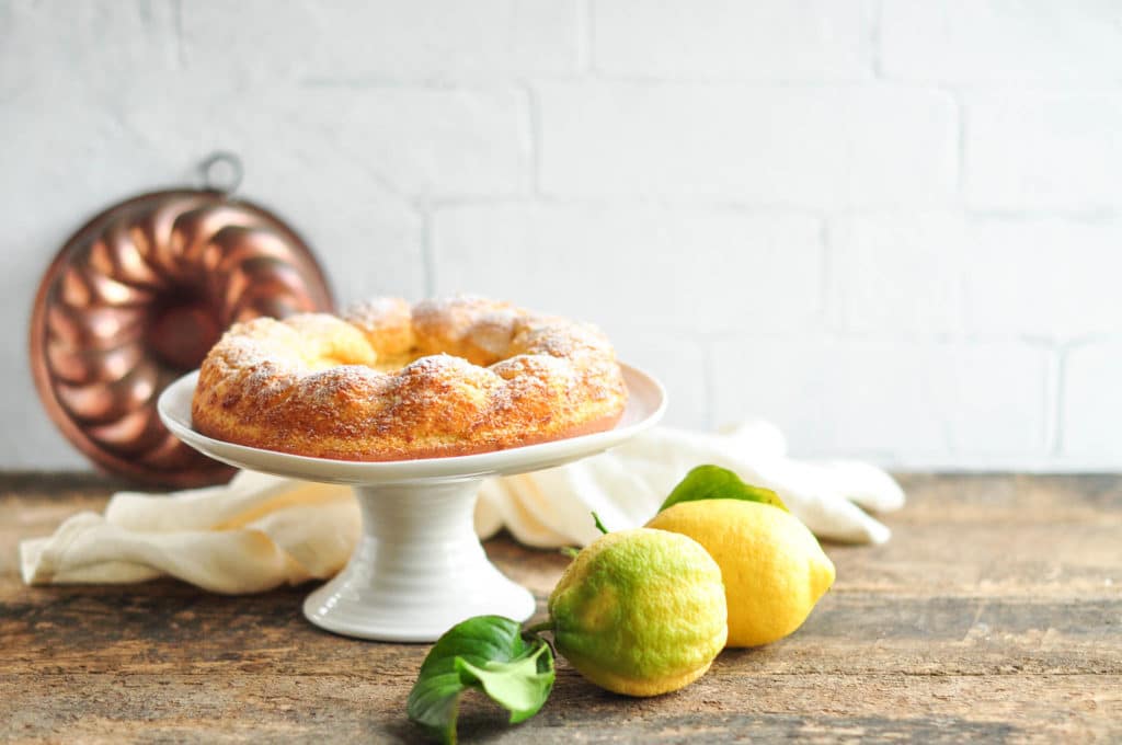 gluten-free lemon cake on white cake stand with fresh lemons