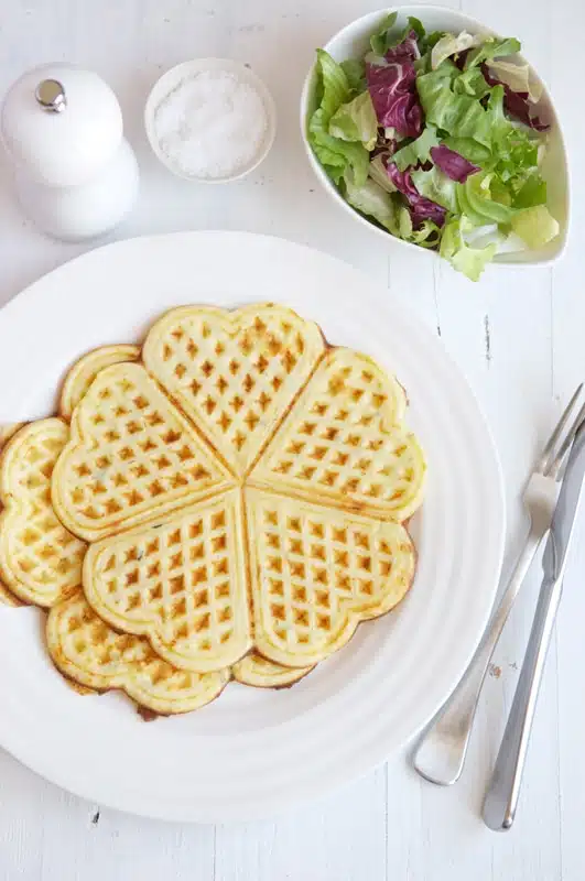 two cheese waffles on white plate with cutlery, salt and pepper