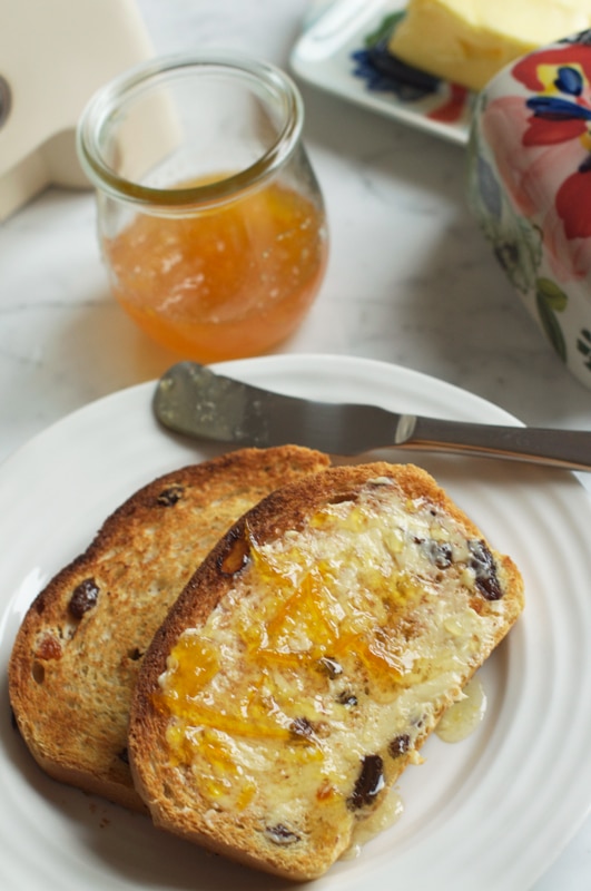 slices of fruit loaf with butter and marmalade on white plate