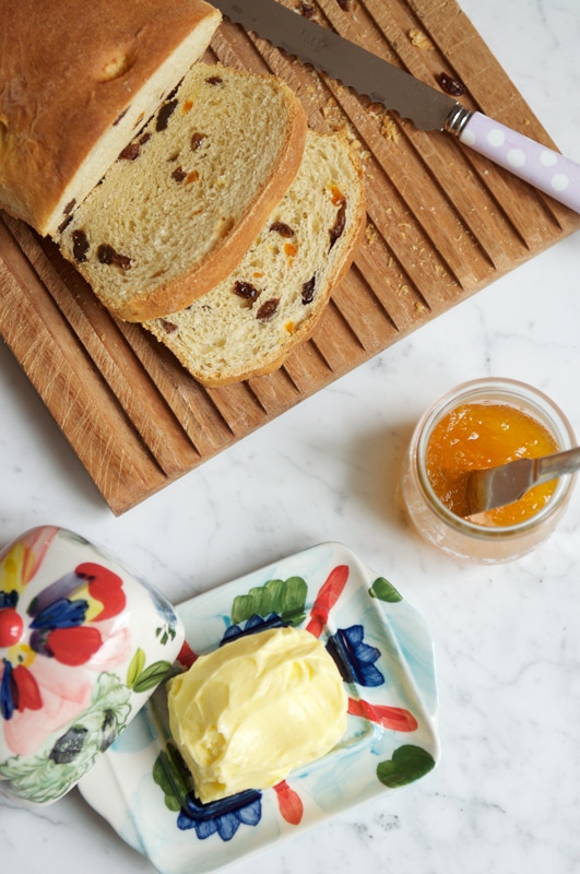 slices of fruit loaf on wooden bread board with butter dish and jar and marmalade