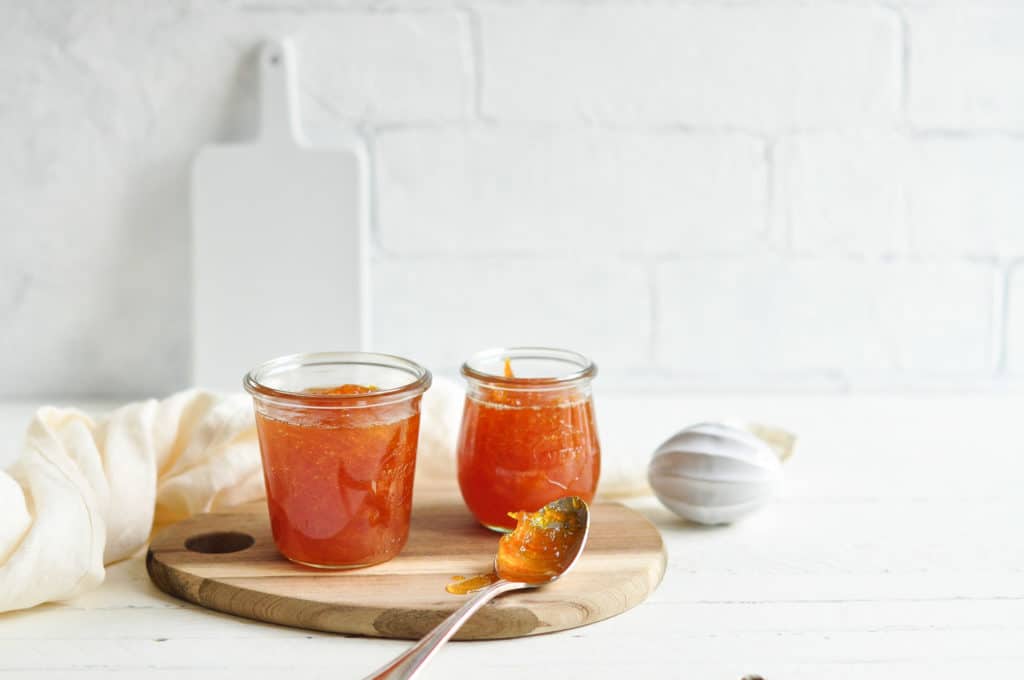 jars of orange marmalade with spoon of marmalade on wooden board
