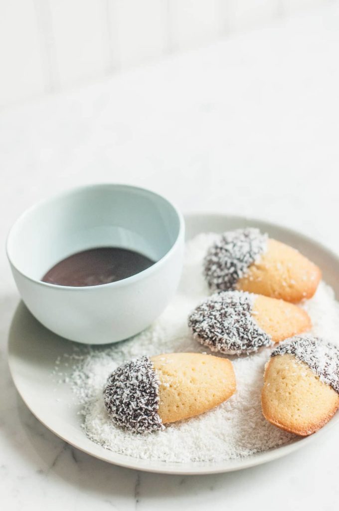 lamington madeleines in bowl of coconut with blue bowl of melted chocolate