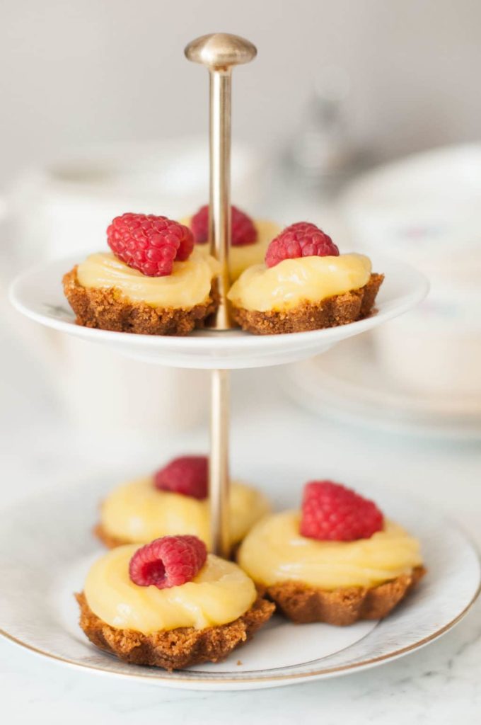 lemon curd tarts decorated with raspberries on small tiered cake stand