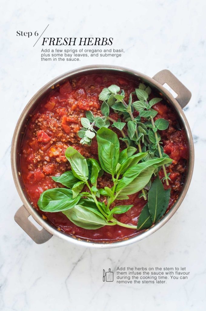 how to make spaghetti bolognese - pan of bolognese sauce with fresh basil, oregano and bay leaves