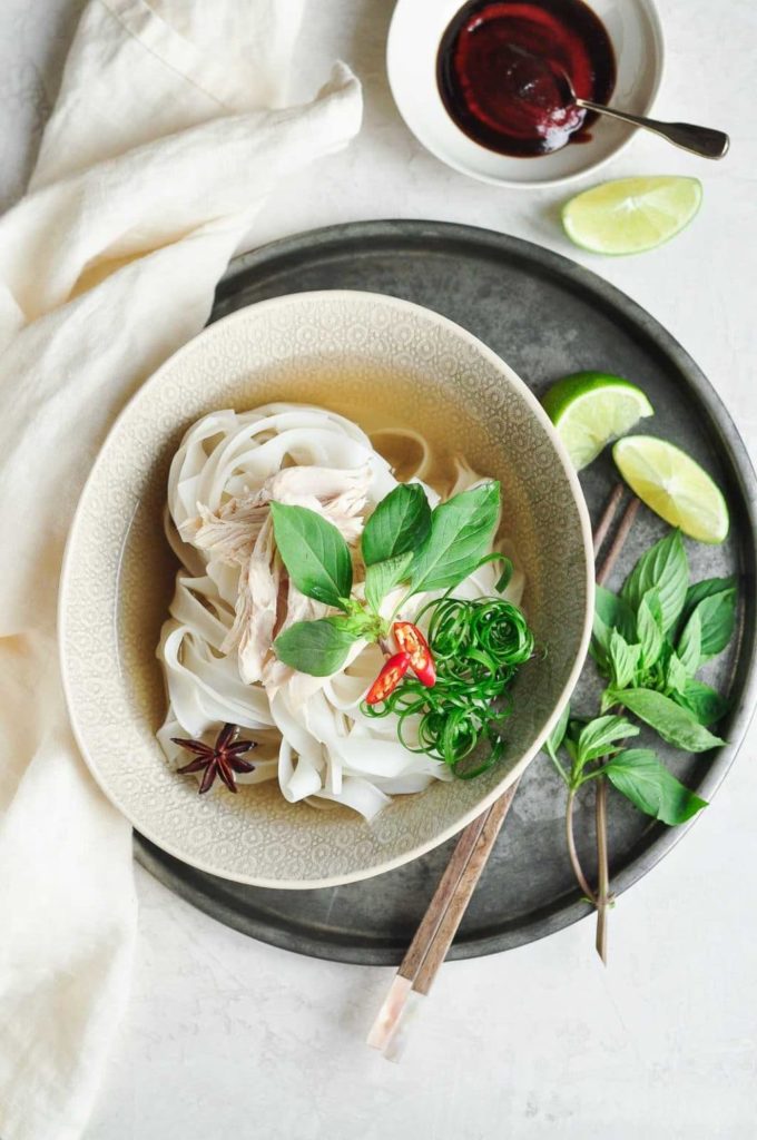 chicken pho recipe with Vietnamese chicken pho in bowl with fresh herbs and chillies with lime wedges and bowl of sauce