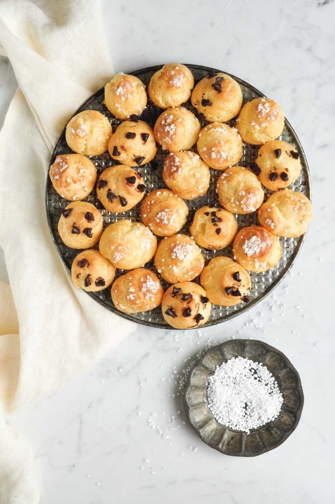 chouquettes (french cream puffs) on metal try with dish filled with pearl sugar