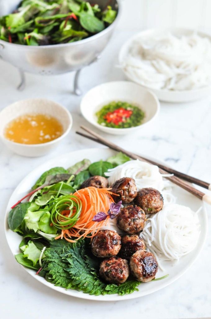 vietnamese pork meatballs on plate with noodles, and bowls of chilli sauce in background