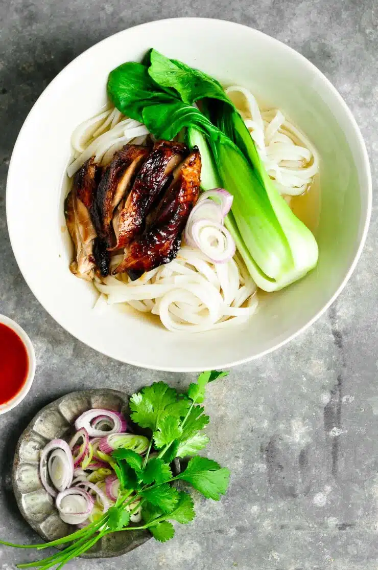 sticky chicken pho with bok choy in bowl with herbs