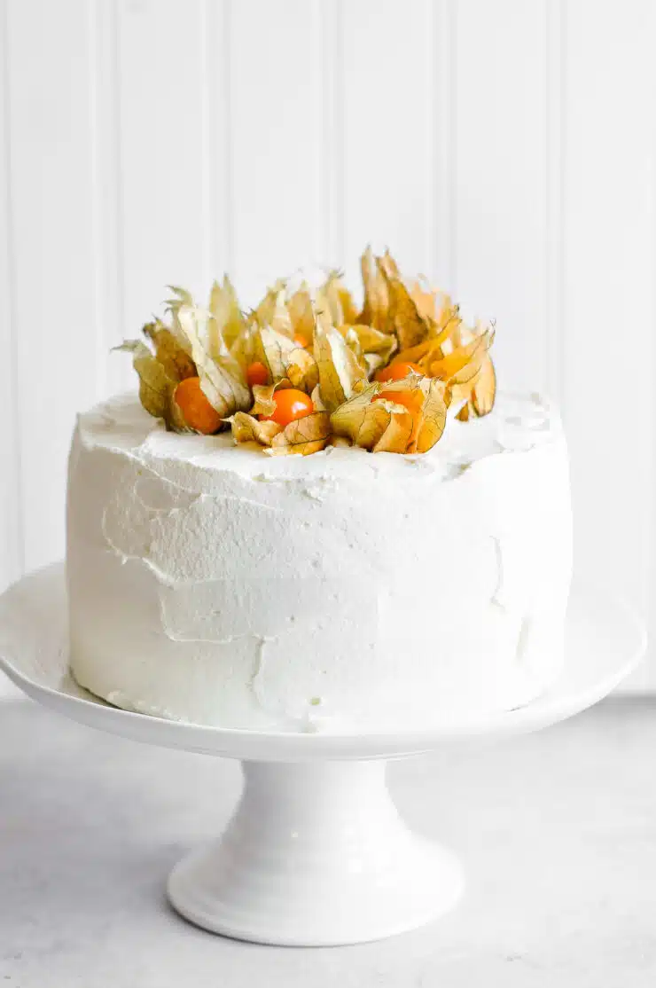 vanilla sponge cake with mascarpone frosting and physalis berries on white cake stand