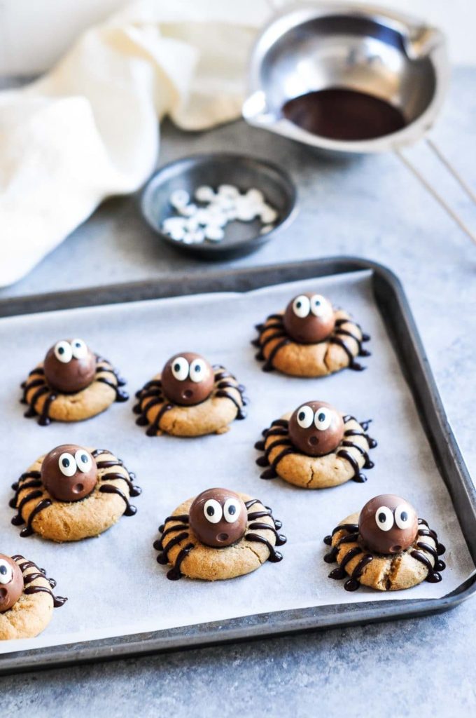 peanut butter spider cookies on baking tray with melted chocolate in background