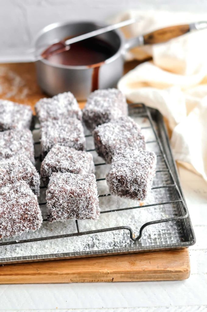 lamingtons on wire rack with pan of chocolate icing