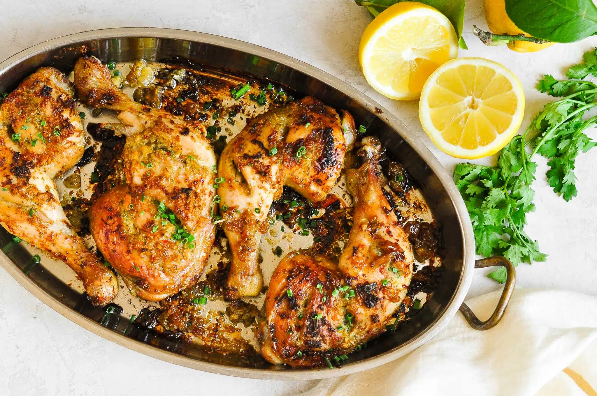 grilled thai chicken in roasting pan with lemon wedges and coriander