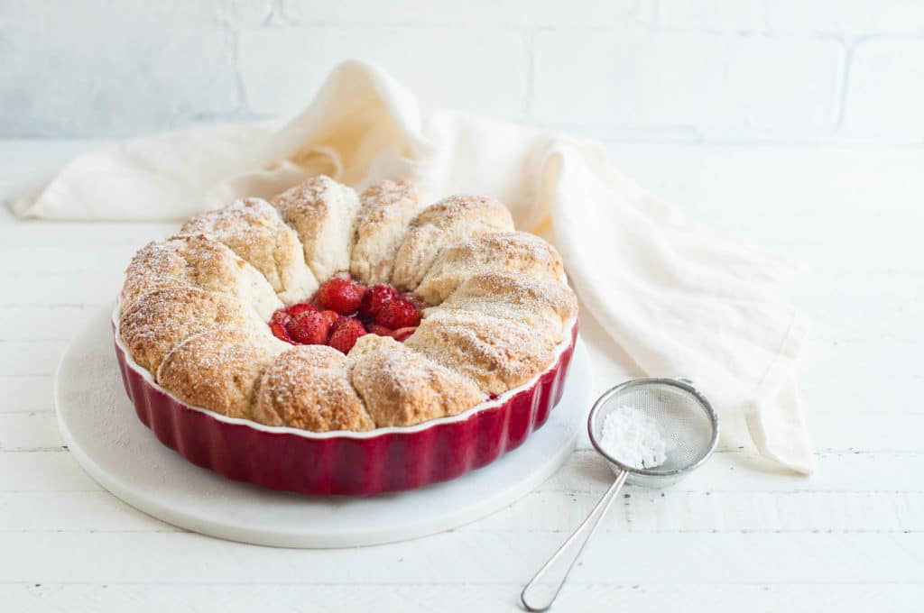 strawberry cobbler in red baking dish with icing sugar sieve