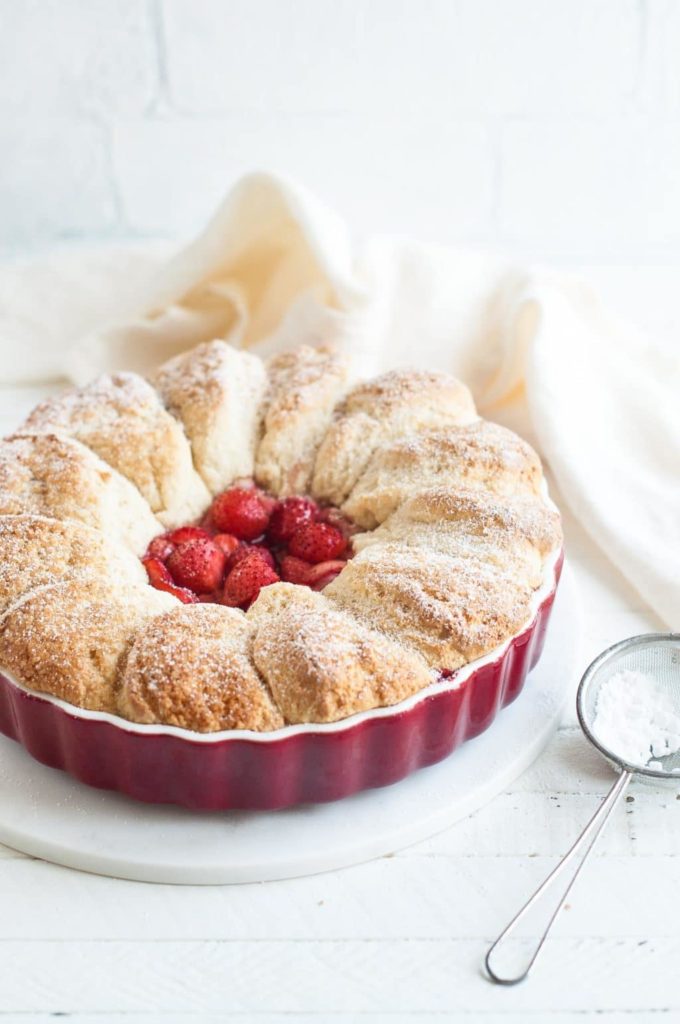 strawberry cobbler in red baking dish with icing sugar duster