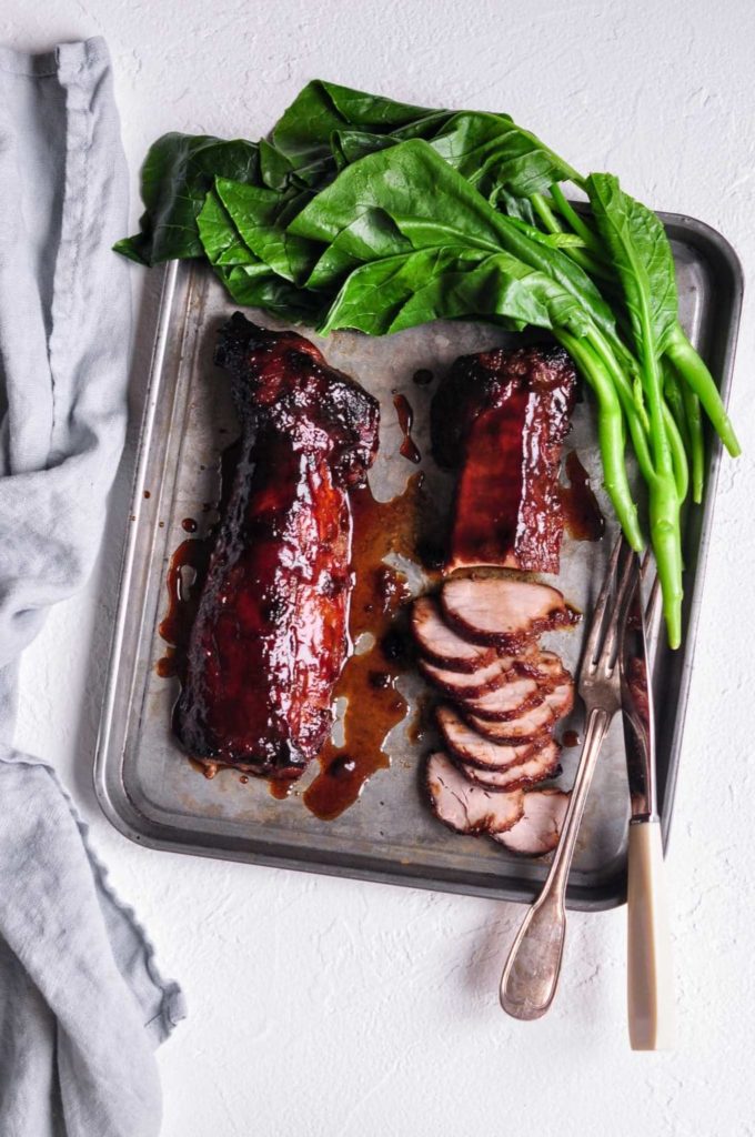 char siu pork sliced on metal tray with green vegetables and cutlery