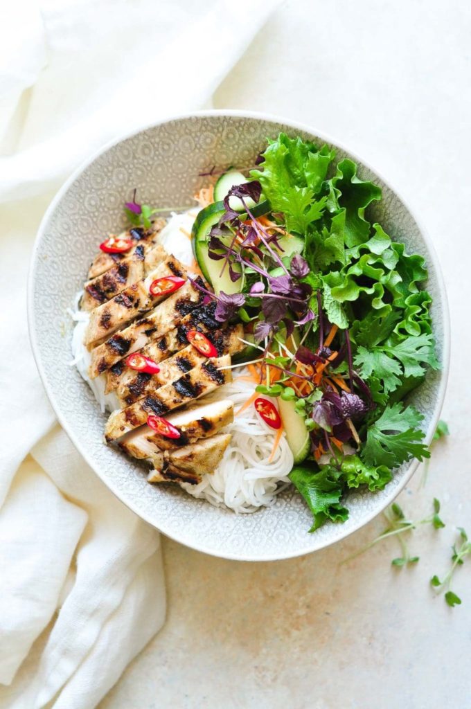 sliced grilled chicken on bowl with noodles, salad and herbs