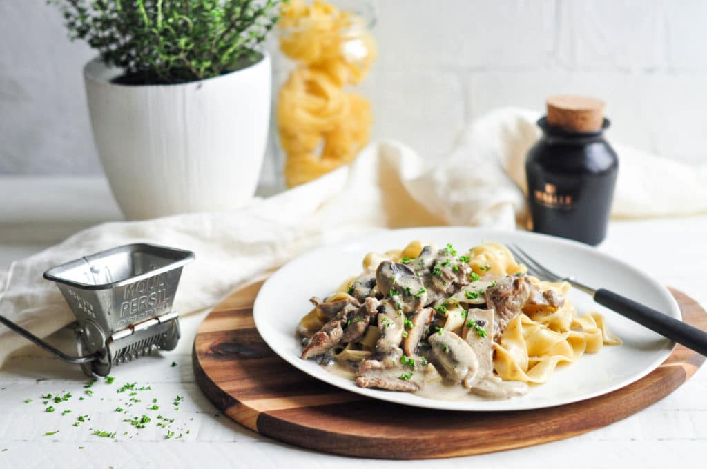beef stroganoff with pasta on plate on wooden board