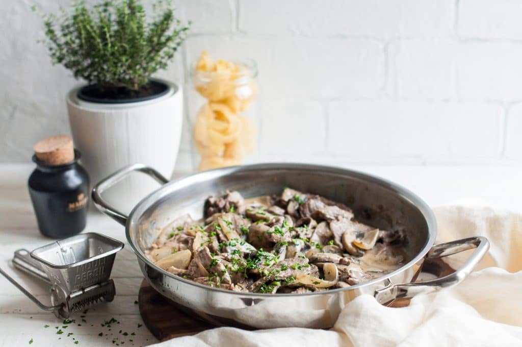 beef stroganoff in large saucepan with white napkin and pot of herbs