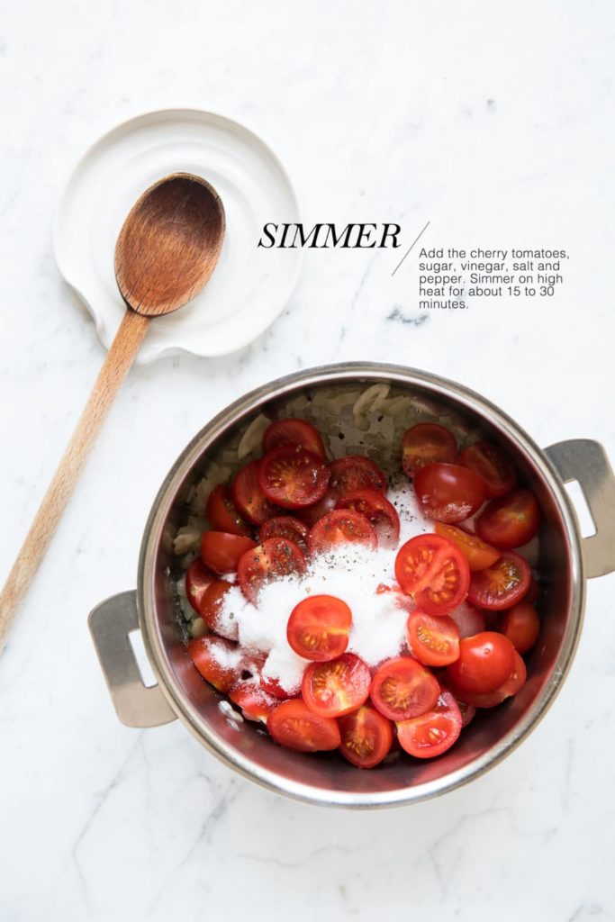 chopped cherry tomatoes in a saucepan with a wooden spoon on white spoon rest