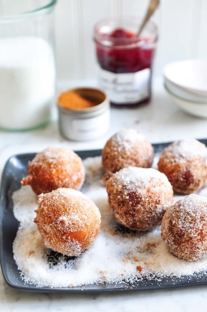 cinnamon doughnuts rolled in cinnamon sugar on large plate with jar of jam in background