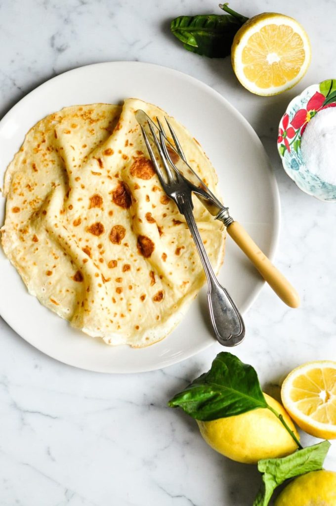 french crepe on plate surrounded by sliced lemons