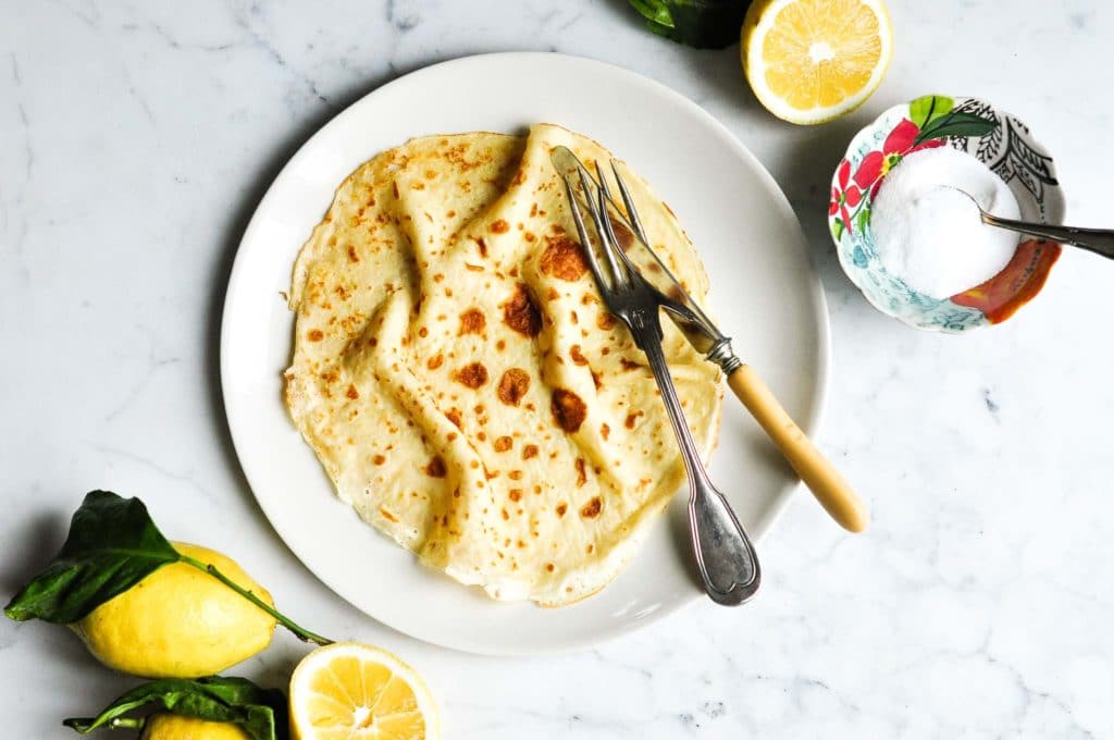 french crepe on plate with knife and fork and sliced lemons on marble table
