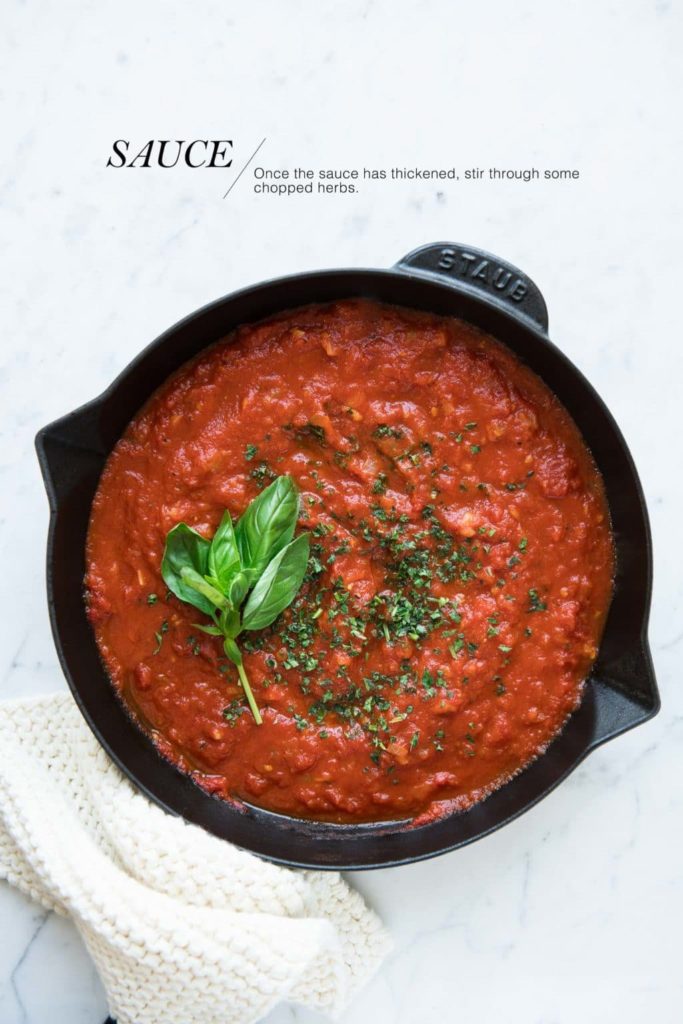 cooked marinara sauce in black skillet with basil leaves and chopped herbs