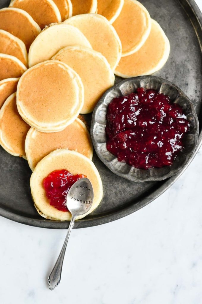 pikelets on a metal tray with a spoonful of jam