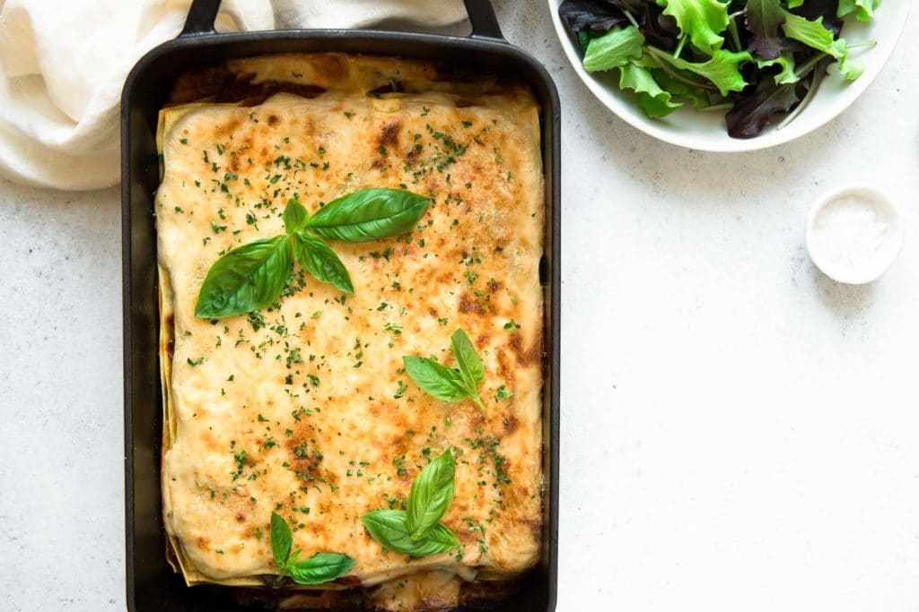 spinach lasagna in black baking dish with plate of salad