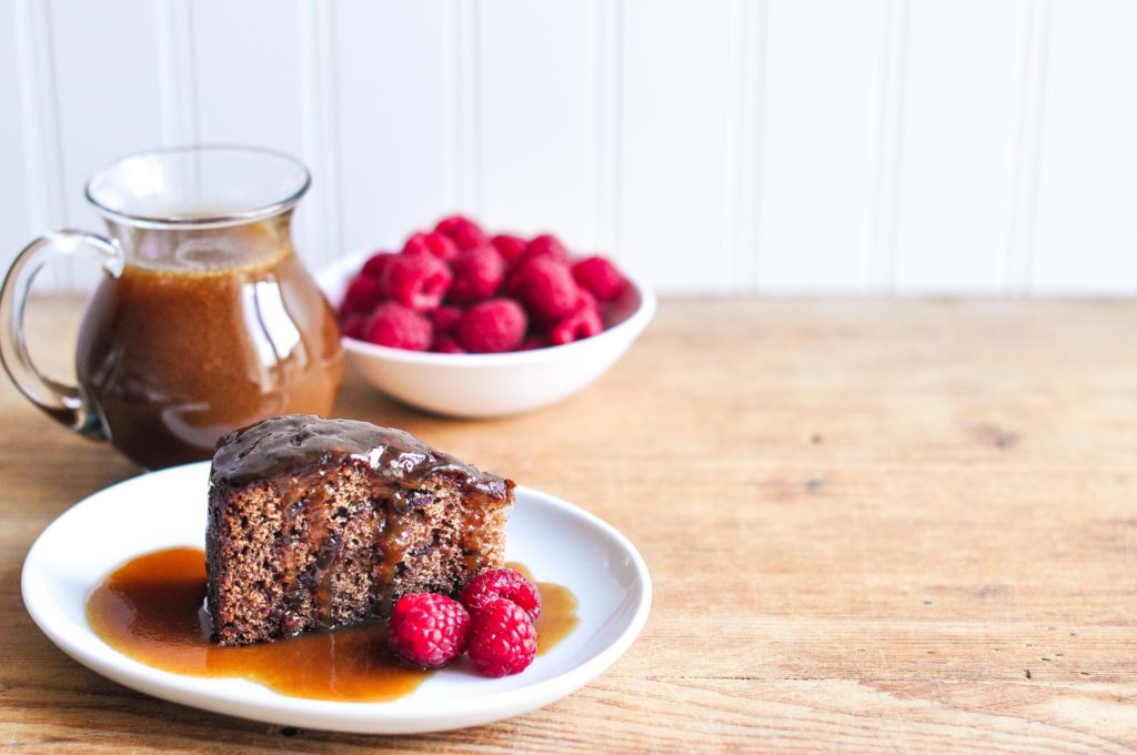 Slice of sticky date pudding with butterscotch sauce and raspberries