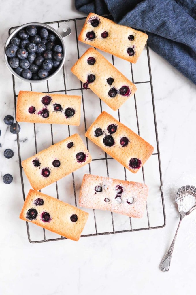 blueberry financier cakes on wire rack with fresh blueberries on the side