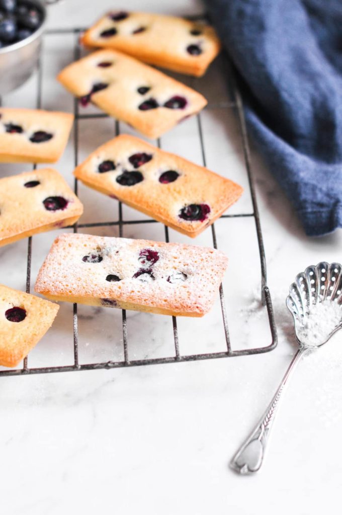 financiers with blueberries on wire rack with vintage icing sugar spoon