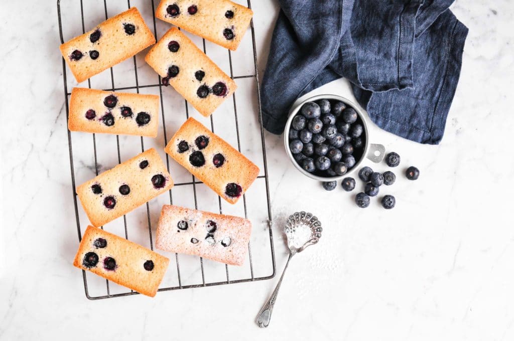 blueberry financier cakes on wire rack with fresh blueberries in bowl