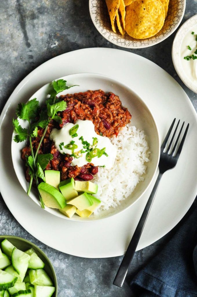 chilli con carne with beans in bowl with rice, sour cream and avocadoes