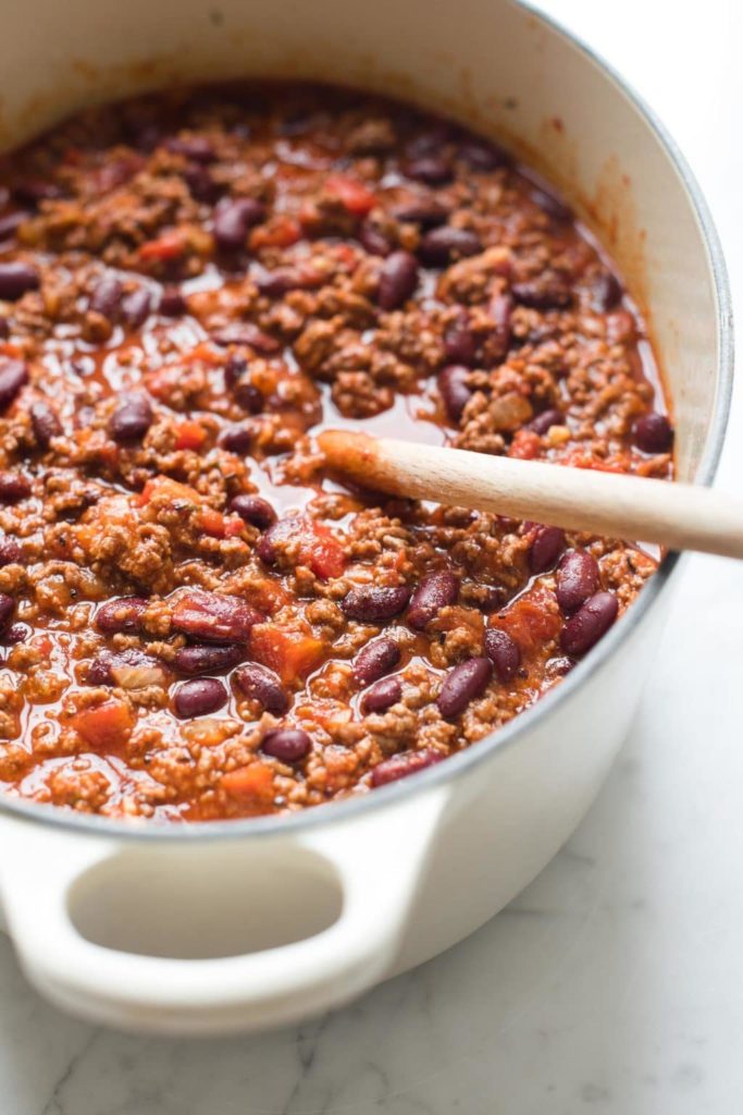 chilli con carne with kidney beans in cast iron pan with wooden spoon