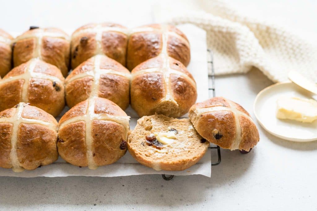 hot cross buns on wire rack with one split open and spread with butter