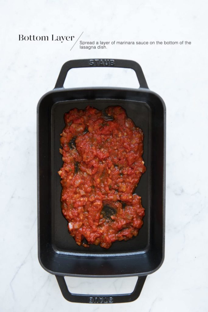 marinara sauce in the bottom of black cast iron lasagna dish