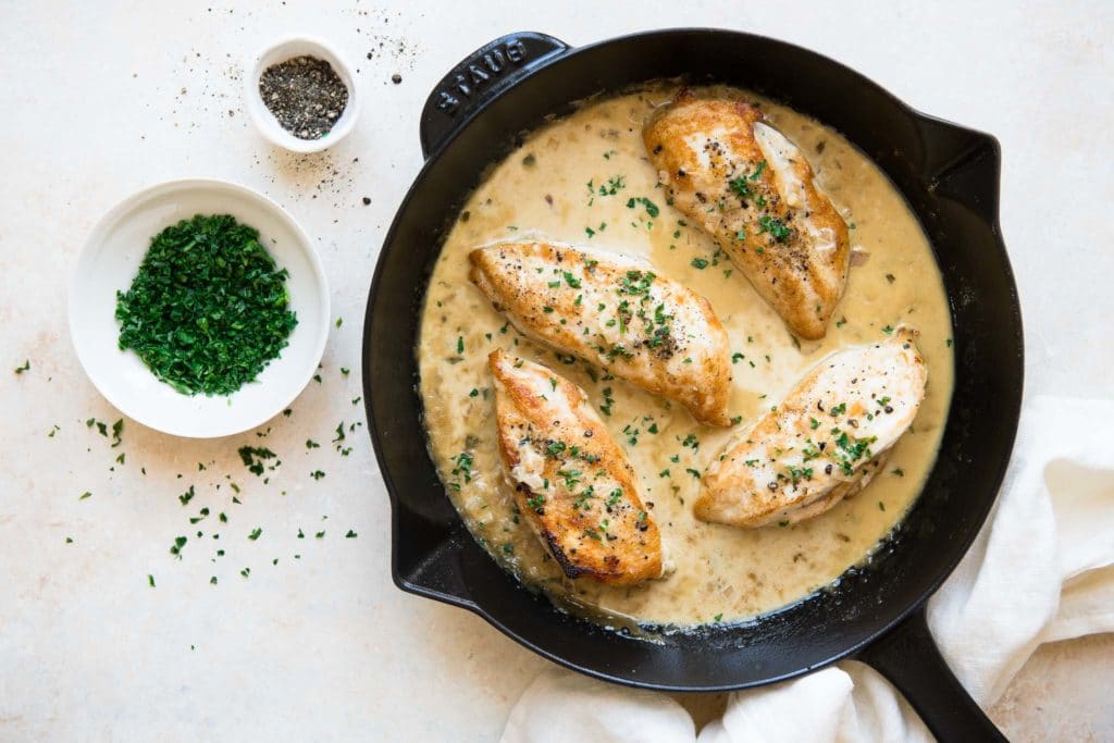 creamy tarragon chicken in black skillet with bowl of herbs and black pepper