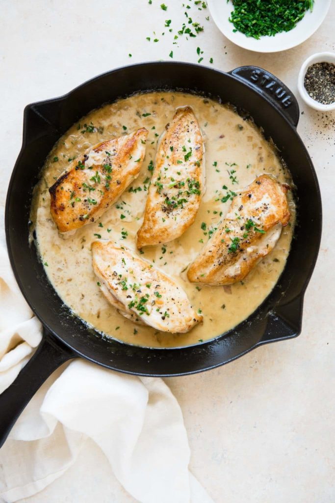 creamy tarragon chicken in cast iron skillet with chopped herbs and pepper