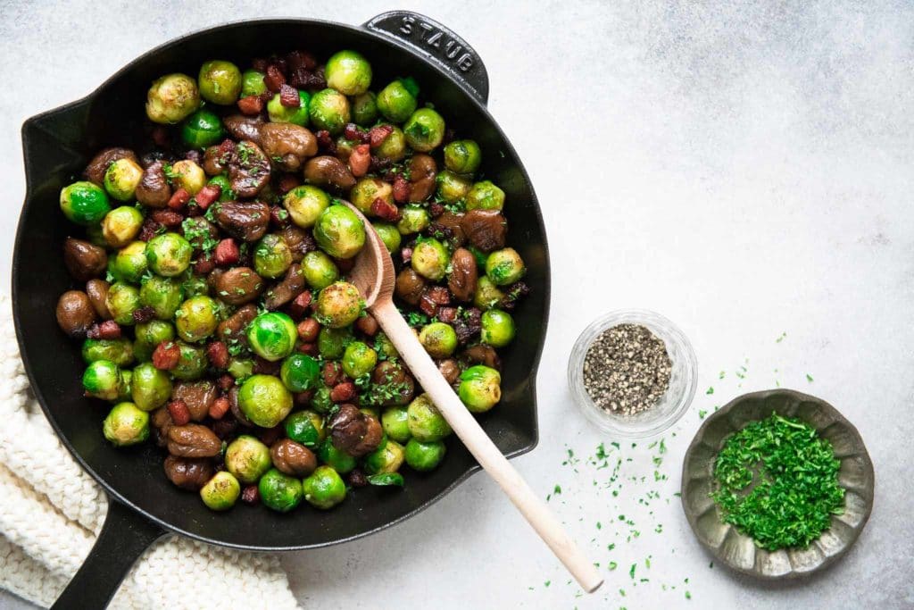 brussels sprouts with chestnuts and pancetta in skillet with wooden spoon