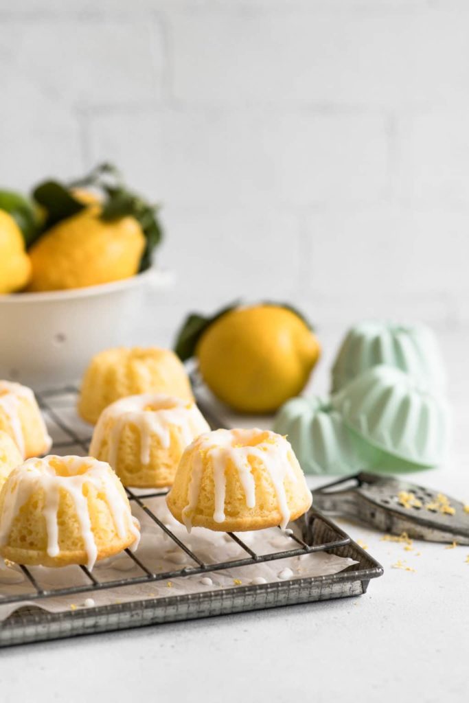lemon bundt cakes with lemon glaze on wire rack with fresh lemons in background