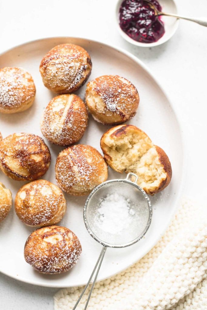 aebleskivers dusted with icing sugar on a plate with raspberry jam in small bowl