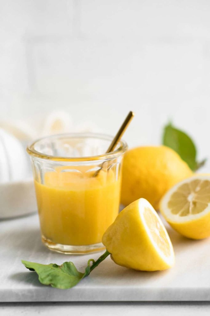 lemon curd in glass jar on marble board with fresh lemons