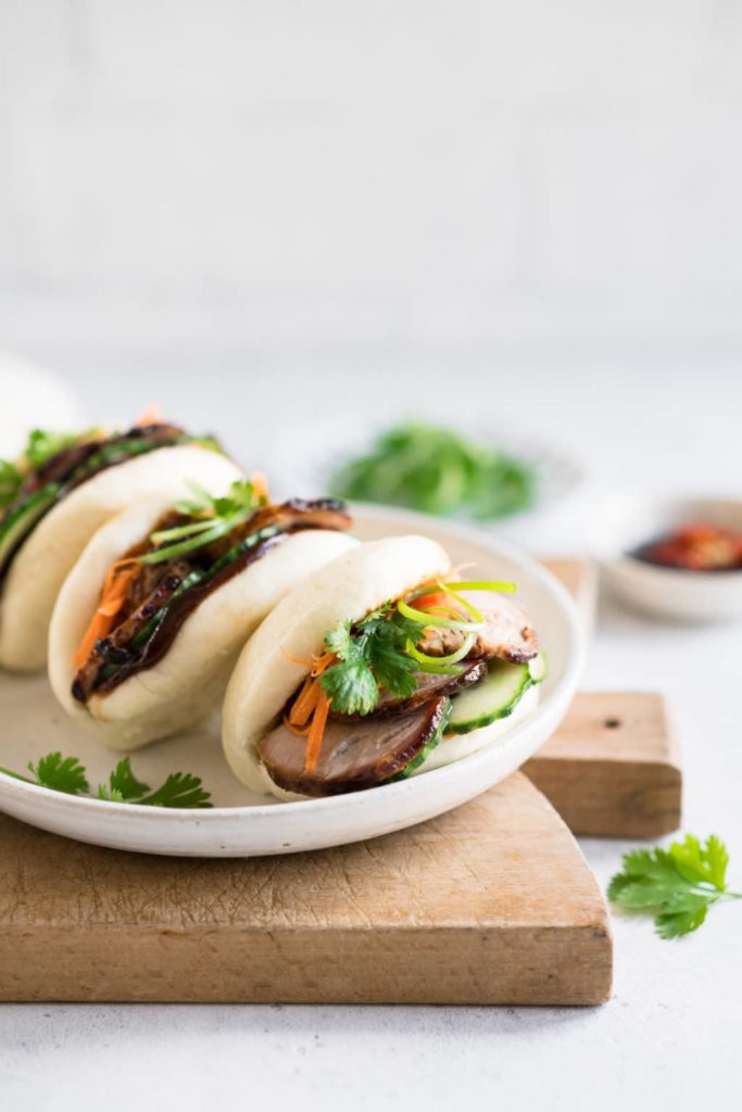 sticky pork bao buns garnished with quick pickled carrots and quick pickled cucumbers