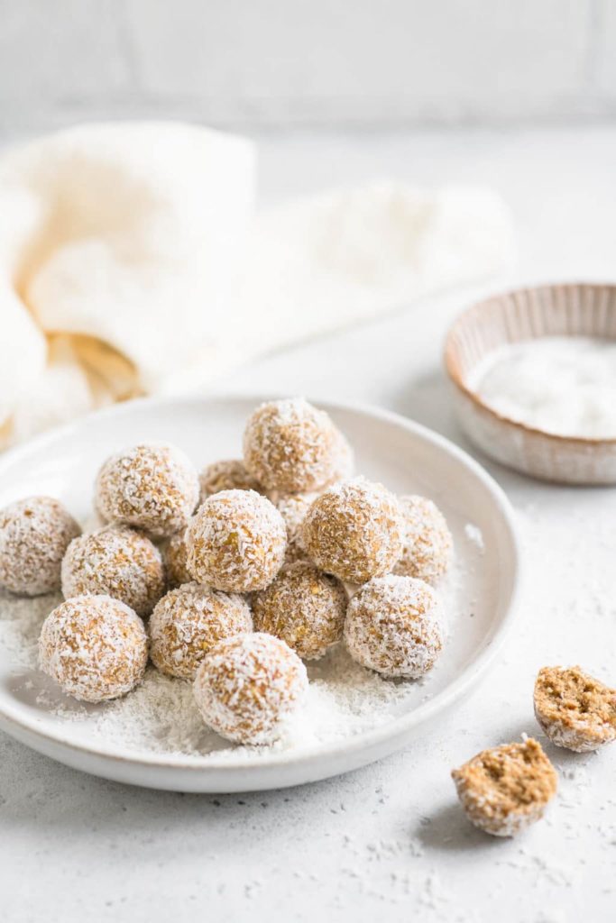 apple pie bliss balls on white plate sprinkled with coconut