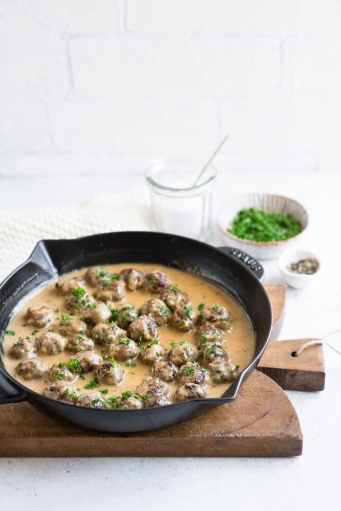 swedish meatballs in skillet on wooden board with fresh herbs